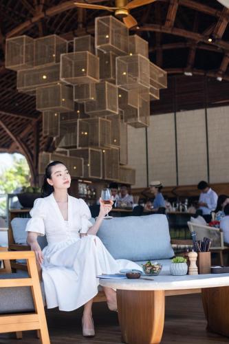 a woman sitting on a couch holding a glass of wine at New World Hoiana Beach Resort in Hoi An
