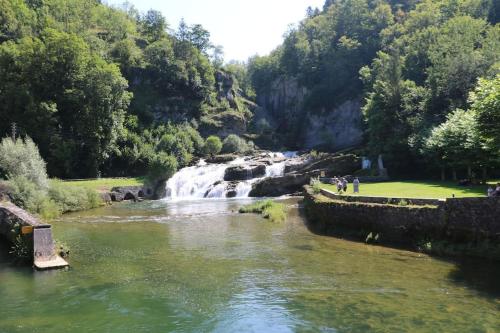 a river with a waterfall and people standing next to it at Au Coeur du Jura, Logement au calme in Champagnole