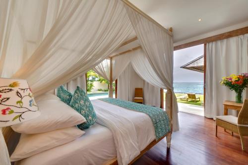 a bedroom with a canopy bed with a view of the ocean at SIRI MENDIRA BEACH VILLAS (Villa Angsoka, Villa Bakung and Villa Cempaka) in Candidasa