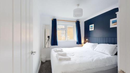 a bedroom with a white bed with blue walls and a window at F60 Atlantic View, Riviere Towans in Hayle
