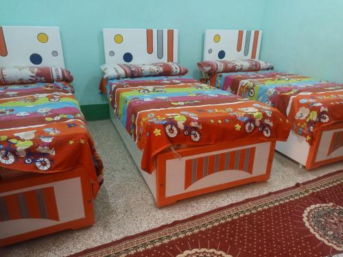 Cette chambre comprend 3 lits avec des draps orange. dans l'établissement Khodrey ka, à Assouan