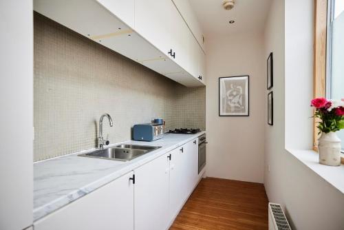 a kitchen with white cabinets and a sink at The Southwark Wonder - Charming 1BDR Flat with Patio in London