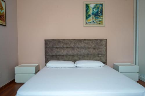 Lovely apartment in the heart of Tirana في تيرانا: غرفة نوم بسرير ابيض مع مواقف ليلتين