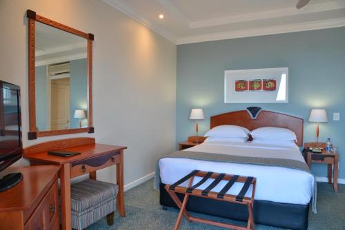 una camera con letto, scrivania e specchio di Courtyard Hotel Gqeberha a Port Elizabeth