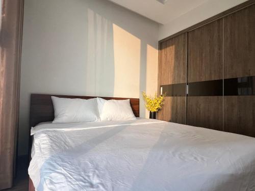 um quarto com uma cama branca e um armário de madeira em Lilyhome - Service Apartments of Vinhomes Metropolis near Lotte em Hanói