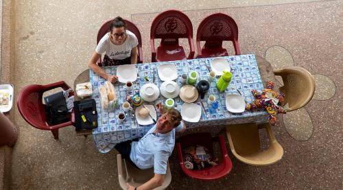 zwei Männer sitzen an einem Tisch mit Tellern und Tassen in der Unterkunft Sign of Silence Hostel in Kumasi