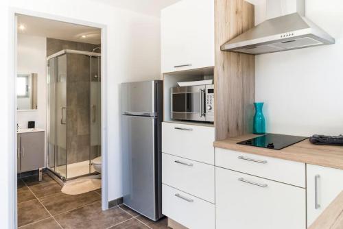 une cuisine avec des armoires blanches et un réfrigérateur en acier inoxydable dans l'établissement Studio en pierre U Pinu, 2 personnes, Muratello, 6 Kms de Porto Vecchio, à Porto-Vecchio