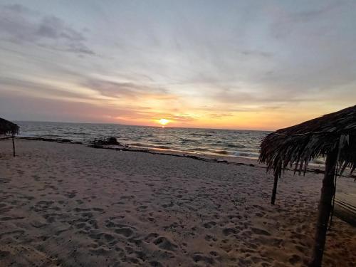 una puesta de sol en la playa con una sombrilla de paja en Akwaba Chez les Filles en Mahajanga