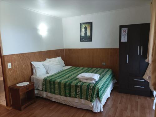 a small bedroom with a bed with a green blanket at Cabañas MANA NUI INN in Hanga Roa