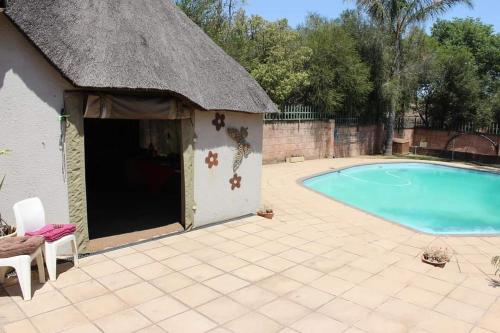 a small swimming pool with a thatch roof at Swartbessie Geusthouse in Krugersdorp