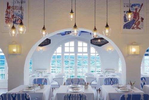 ein Esszimmer mit weißen Tischen und einem großen Fenster in der Unterkunft Hostal de la Gavina GL - The Leading Hotels of the World in S'Agaró