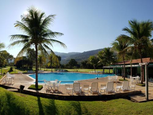 uma piscina com cadeiras brancas e palmeiras em Águas de Santa Bárbara Resort Hotel em Fábrica Santa Bárbara