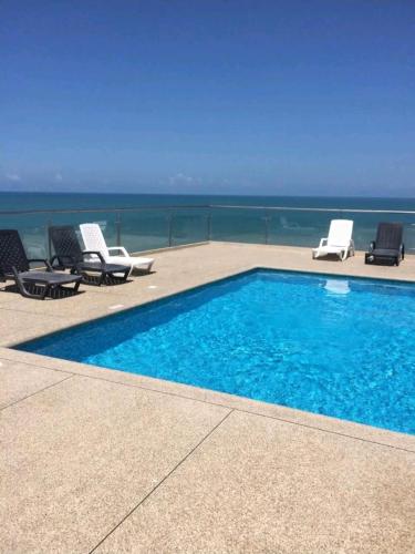 a swimming pool with chairs and the ocean in the background at MAKANA Tonsupa - Suites y Departamentos Familiares - Deluxe Suites in Tonsupa