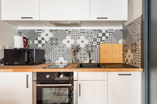 a kitchen with white cabinets and a black and white tile wall at Le Charmant Hypercentre tram design in Saint-Étienne