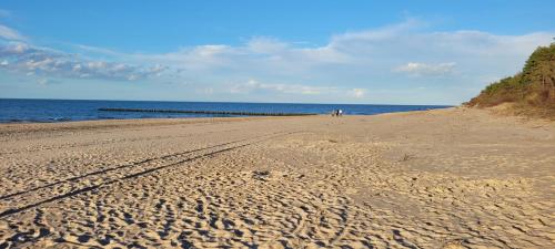 a sandy beach with two people walking on the beach at PINEA Apartments Pobierowo z niesamowitym widokiem na morze oraz jacuzzi w wybranych apartamentach in Pobierowo