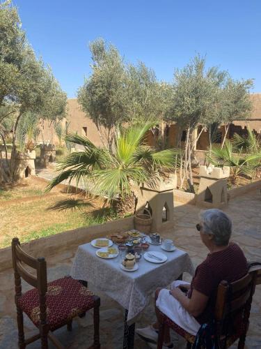 an older woman sitting at a table with food on it at Kasbah Erg Chebbi in Merzouga