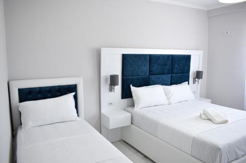 a white bedroom with two beds and a blue headboard at Gimi Apartments Shengjin in Shëngjin