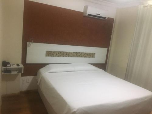 um quarto com uma cama branca e uma parede castanha em Emirates Hotel & Suites em Santana do Livramento