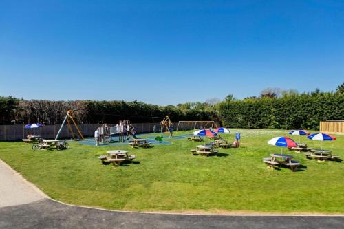 einen Park mit einem Spielplatz mit Tischen und Sonnenschirmen in der Unterkunft Birchington Vale entire holiday home in Westgate-on-Sea