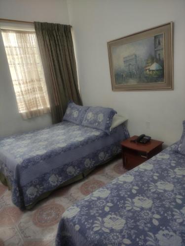a bedroom with two beds and a window and a table at Hotel Bella Montaña in Manizales