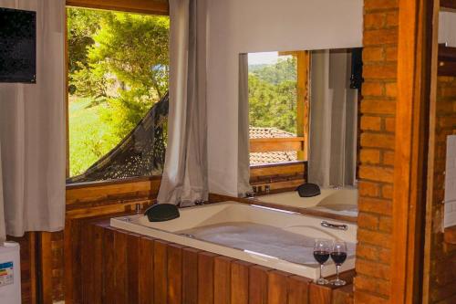 a bath tub with a window and two glasses of wine at Chales Edelweiss in Visconde De Maua