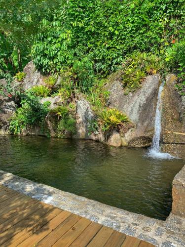 a waterfall in a pool of water with a wooden deck at Casas D'Água Doce - Casa Luz in Ilhabela