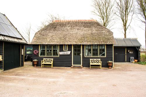 a black house with a straw roof and two chairs at Gastenverblijf De Weldadigheid in Eesveen