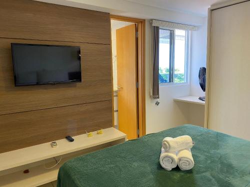 1 dormitorio con TV y 1 cama con toallas en Bela Hospedagem - At Sul - Flat com vista para o mar a 80m do Bar do Cuscuz, en João Pessoa