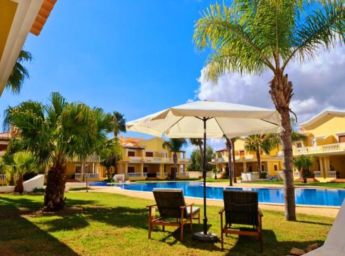 een zwembad met 2 stoelen en een parasol en palmbomen bij Homefield Gardens by HnM in Conceição