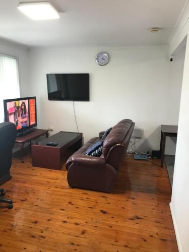 a living room with a brown leather couch and a tv at Fragrant Homes-68B independent aircon room, with 65’TV, queen size beds, rest sofa, built in wardrobe in Doonside