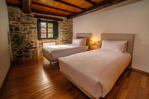 a bedroom with two beds and a stone wall at Casa Grande do Soxal in Cesuras