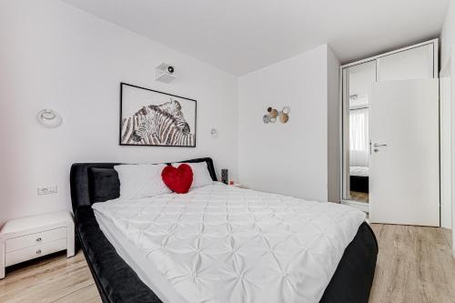 a white bedroom with a bed with a red heart pillow at ARI Cinema Apartament in Arad