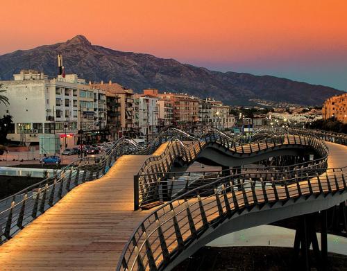 eine hölzerne Promenade, die zu einer Stadt bei Sonnenuntergang führt in der Unterkunft Hostal La Colonia in Marbella