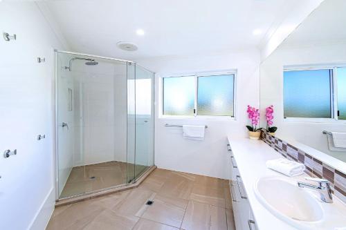 Baño blanco con ducha de cristal y lavabo en 10 Mona Vista Court en Coolum Beach