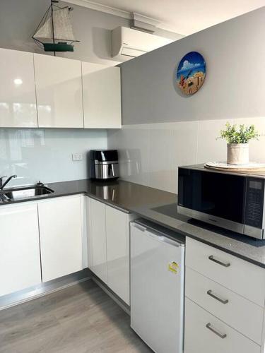 a kitchen with white cabinets and a black microwave at Snapper Villa - Seaside in Urangan