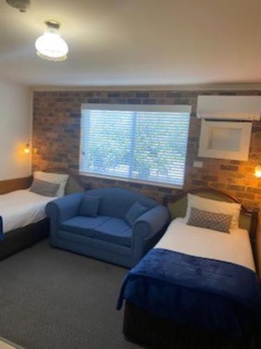 a room with two beds and a blue couch and a window at Kinross Inn in Cooma
