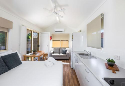 a white bedroom with a bed and a kitchen at Reflections Ballina - Holiday Park in Ballina