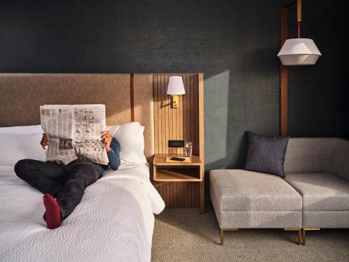 Holiday Inn Chicago O'Hare - Rosemont, an IHG Hotel في روزمونت: شخص يستلقي على سرير ويقرأ جريدة