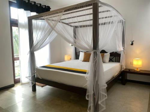 a bedroom with a canopy bed with white drapes at Mango Tree Villa Bentota in Bentota