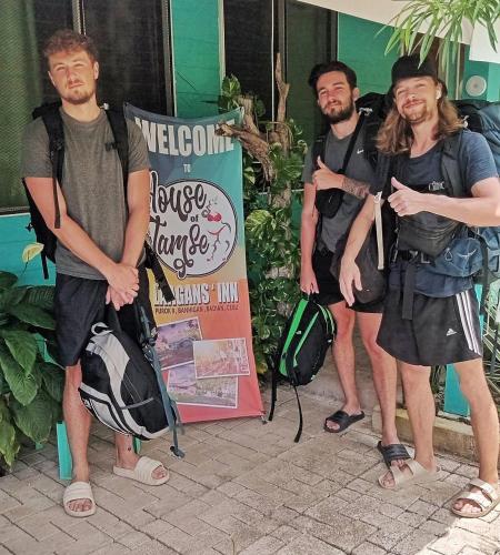 a group of three men standing next to a sign at House of TamSe Laagans ' Inn in Badian