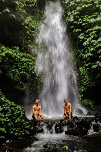 two men sitting on a rock in front of a waterfall at Tastura Homestay in Praya