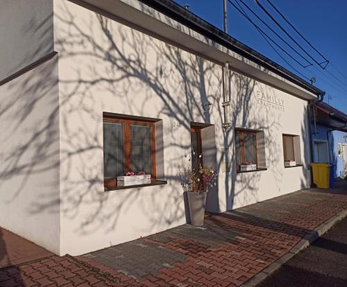 a white building with two windows and a shadow of a tree at Familly Apartmens in Dolní Dunajovice