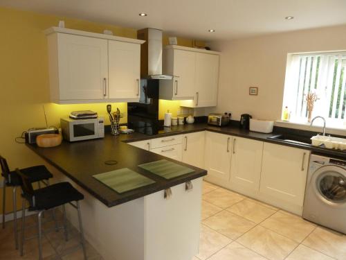 a kitchen with white cabinets and a washer and dryer at Hendre Wen luxury cottage in Betws y Coed in Betws-y-coed