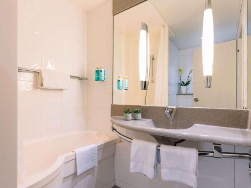 een badkamer met een wastafel, een bad en een spiegel bij Novotel Venezia Mestre Castellana in Mestre