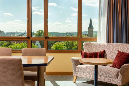 uma sala de estar com cadeiras, uma mesa e janelas em Vienna House by Wyndham Remarque Osnabrück em Osnabrück