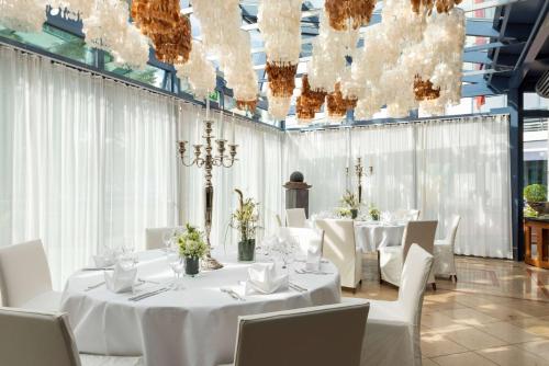 a dining room with white tables and chairs and chandeliers at Vienna House by Wyndham Remarque Osnabrück in Osnabrück