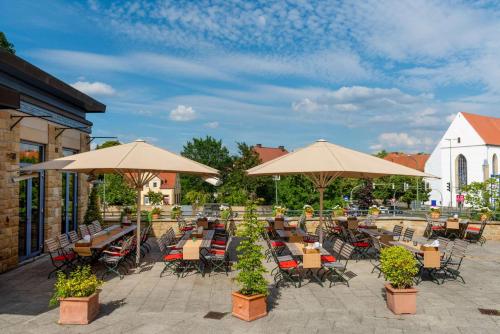 un patio al aire libre con mesas, sillas y sombrillas en Vienna House by Wyndham Remarque Osnabrück en Osnabrück