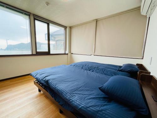 1 dormitorio con 1 cama con sábanas azules y ventanas en Uhome Kamogawa 本館-【ペット可/広い2LDK】, en Kamogawa