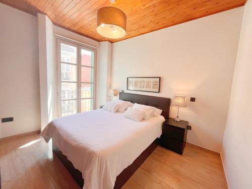 una camera da letto con un grande letto bianco e un soffitto in legno di Homely Málaga Carretería con piscina a Málaga