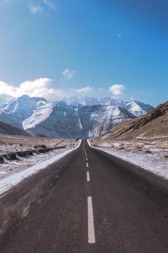 an empty road with snow covered mountains in the distance at Hotel Bergo Residency - Leh in Leh